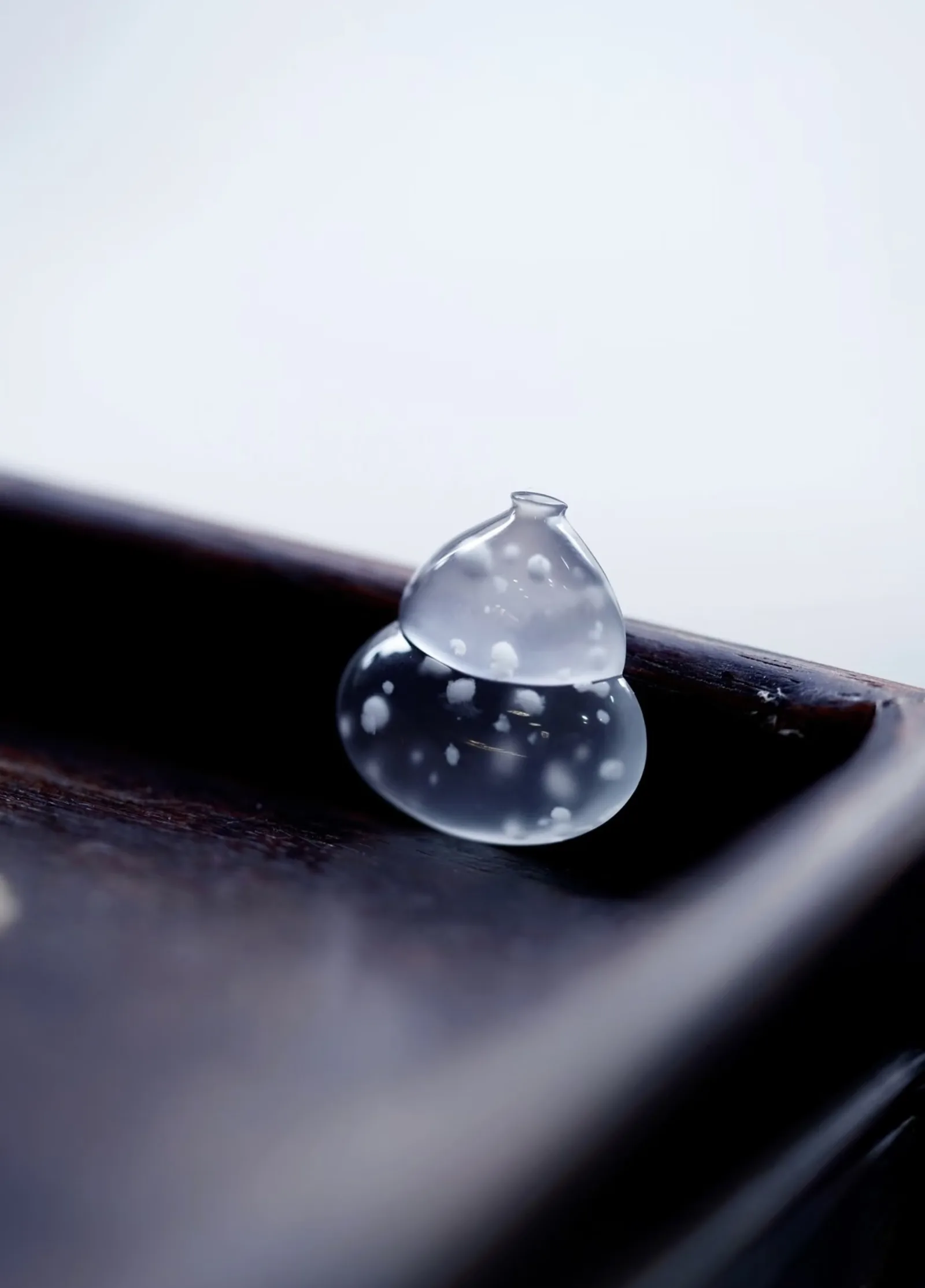 A translucent gourd-shaped gem resting on a dark lacquered wooden tray.