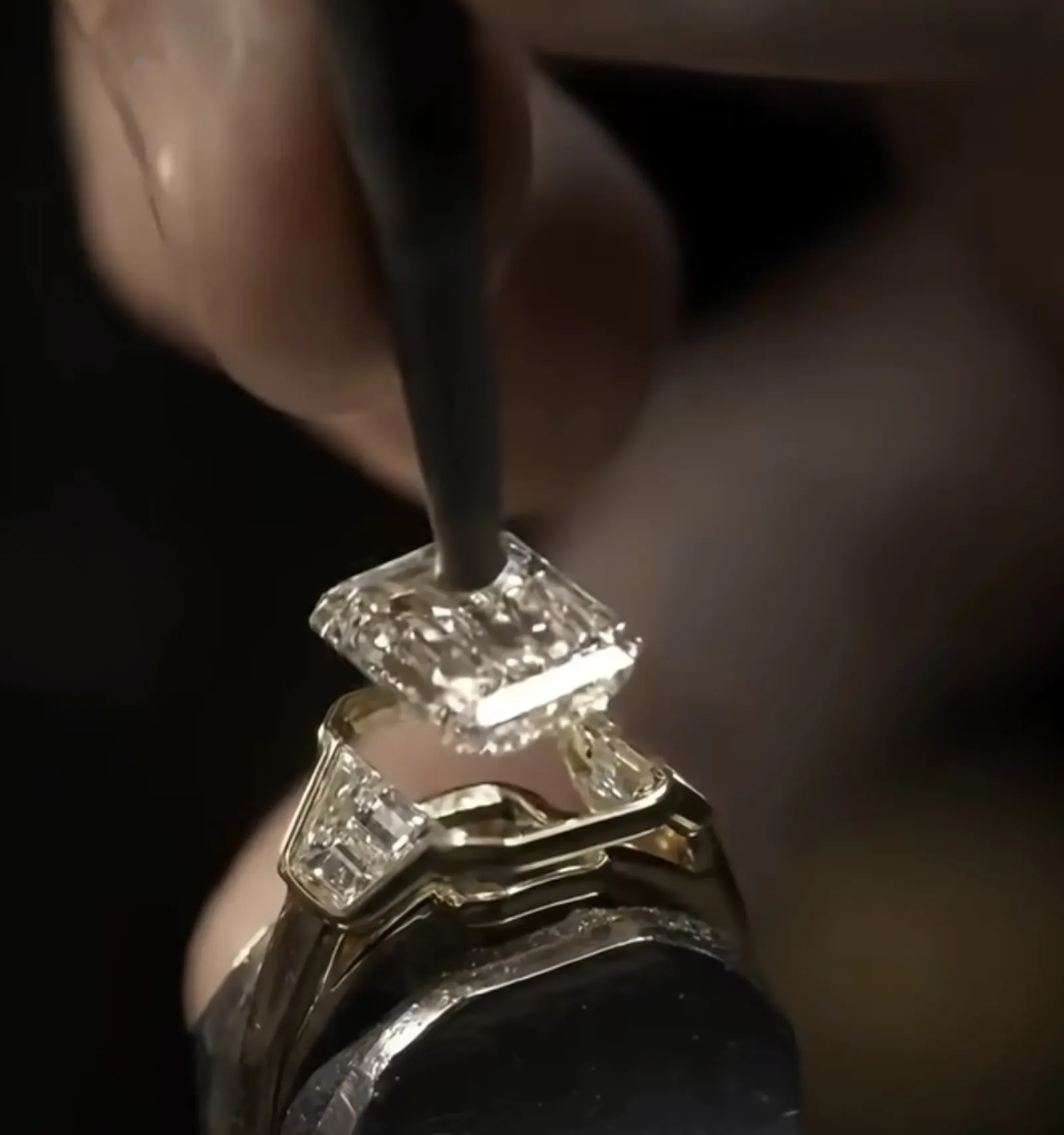 A jeweler's hands setting an emerald-cut diamond into a gold ring — craft in progress.
